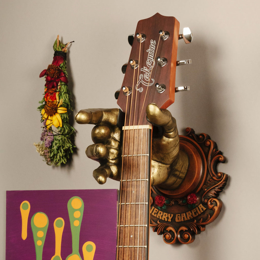 Jerry Garcia Officially Licensed Guitar Hanger from GuitarGrip. On wall with purple artwork and sage. 