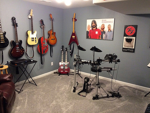 Music room with guitar wall display, black electronic drums set, and Foo Fighter poster. 