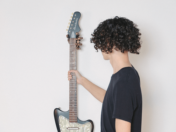 teenage with black curly hair reaching for guitar hanging on wall.