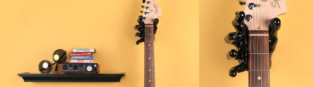 Fender guitar hanging on yellow wall next to a black shelf. 