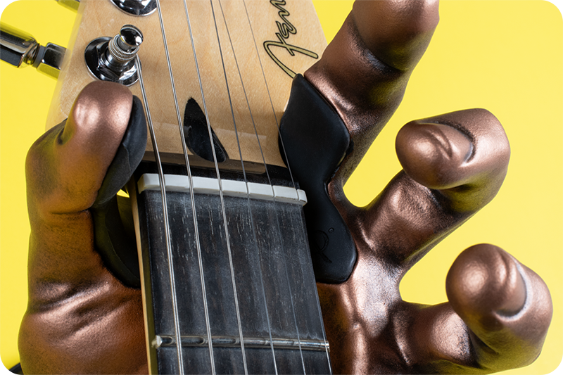 Copper hand guitar hook wall mount on yellow background holding fender guitar. 