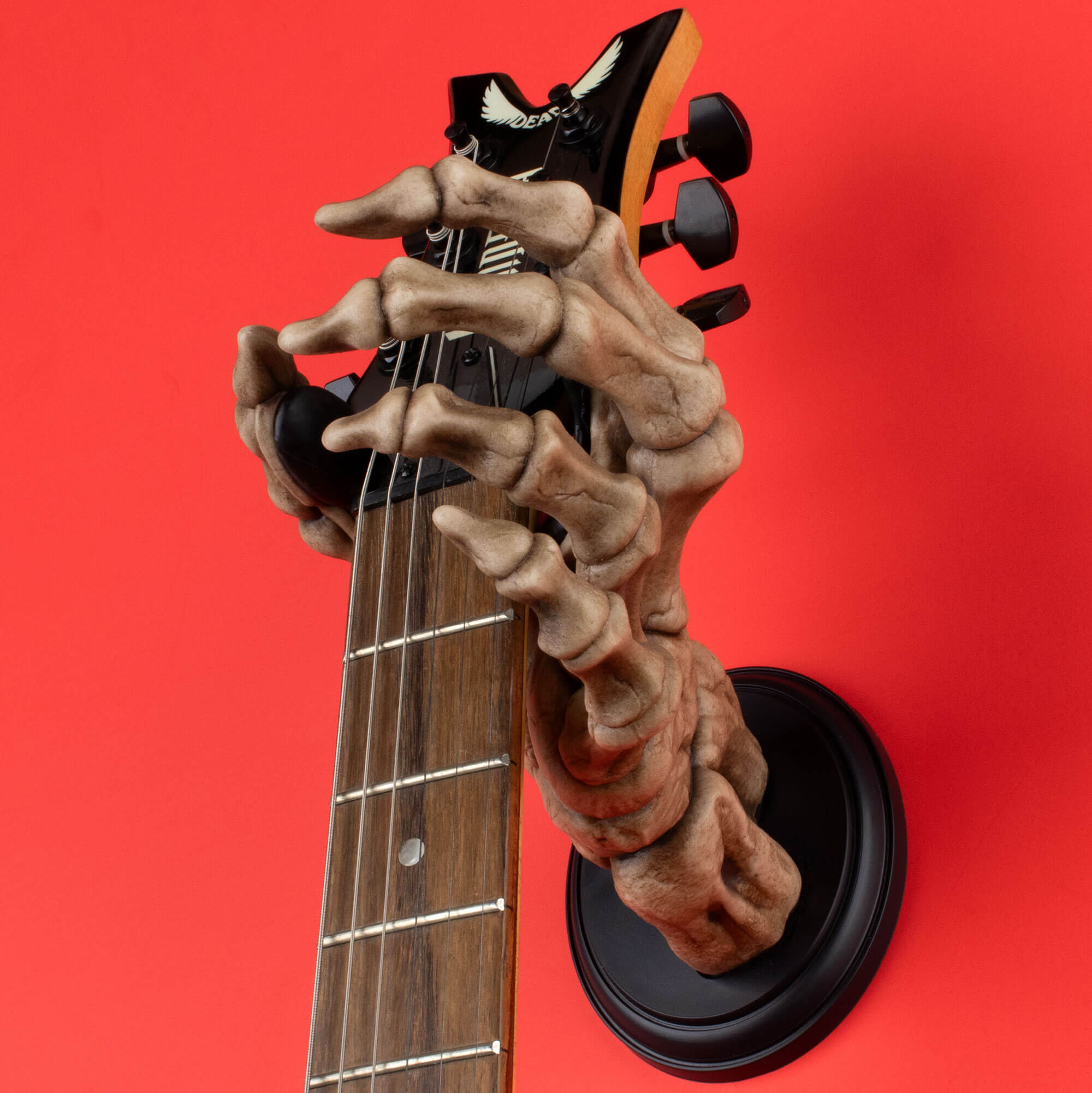 Skeleton hand wall mount on red background holding electric guitar.