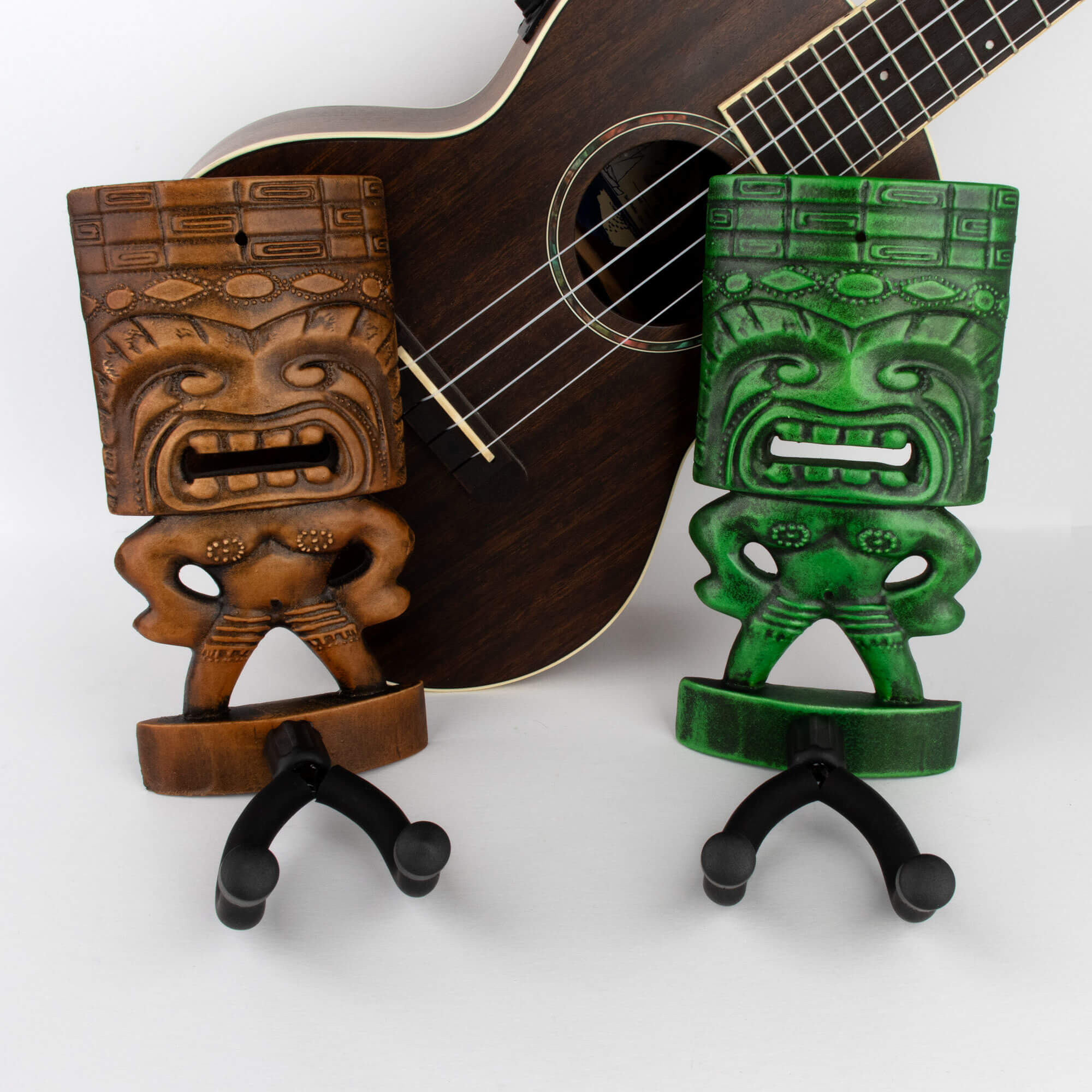 Tiki ukulele wall hangers in green and brown with uke in background. 