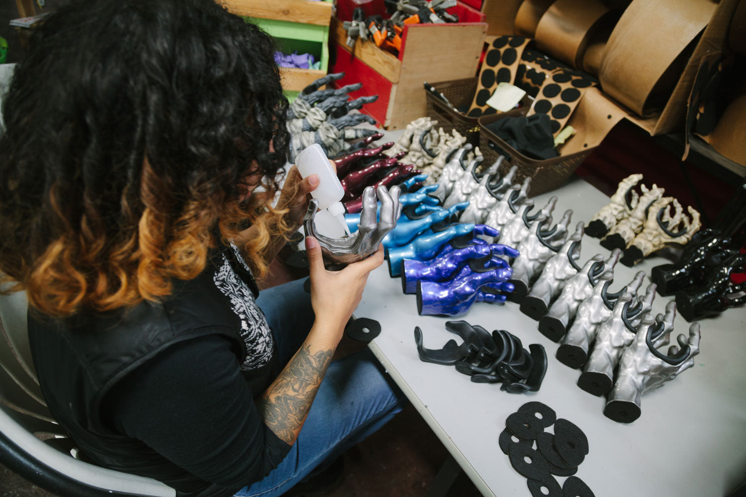 Girl with black curly hair working at a table with hand shaped wall hangers. 