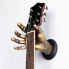 Gold hand holding an electric guitar in the wall. GuitarGrip hand shaped guitar hanger.