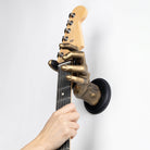 Gold left male hand guitar hanger wall mount holding stratocaster guitar.