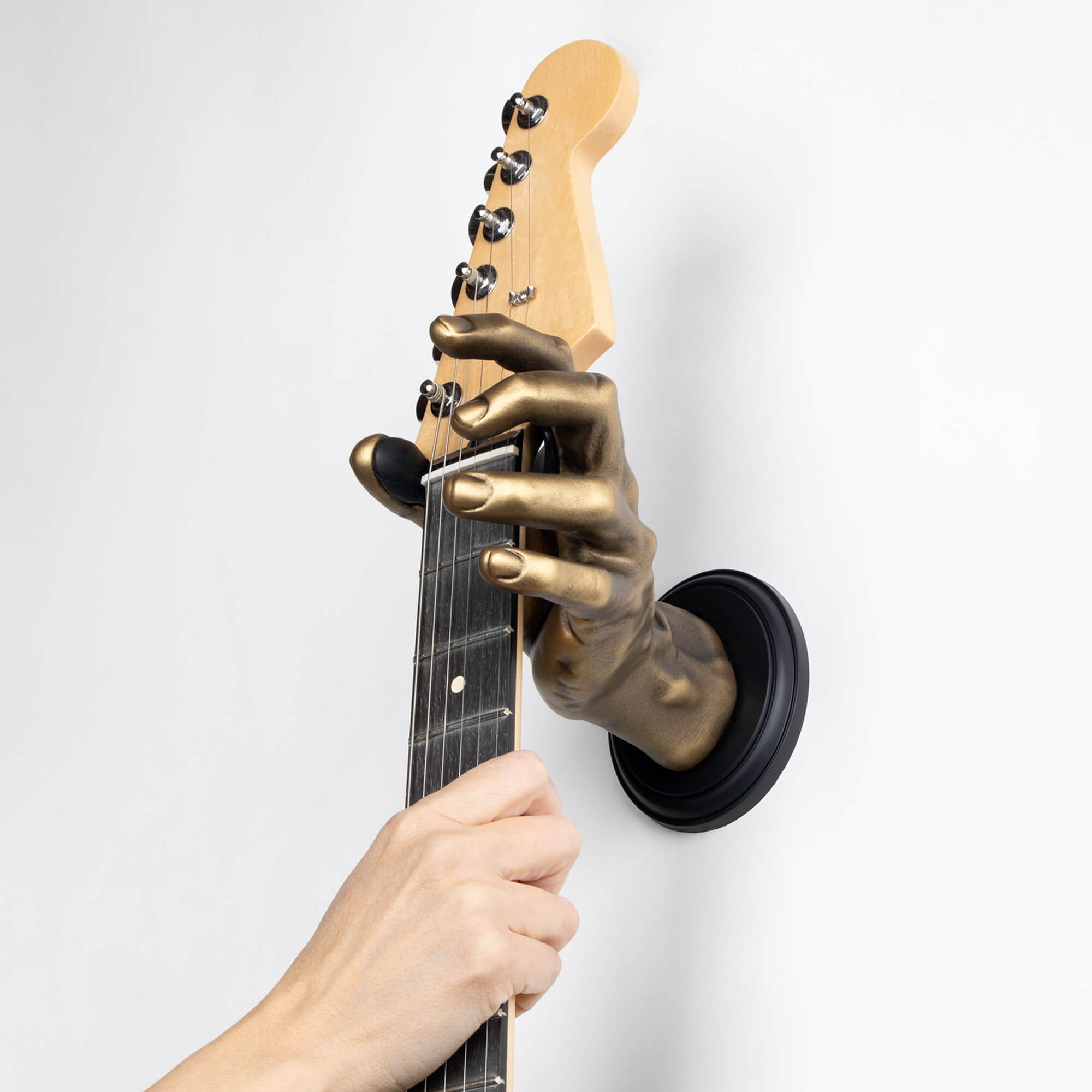 Gold left male hand guitar hanger wall mount holding stratocaster guitar.